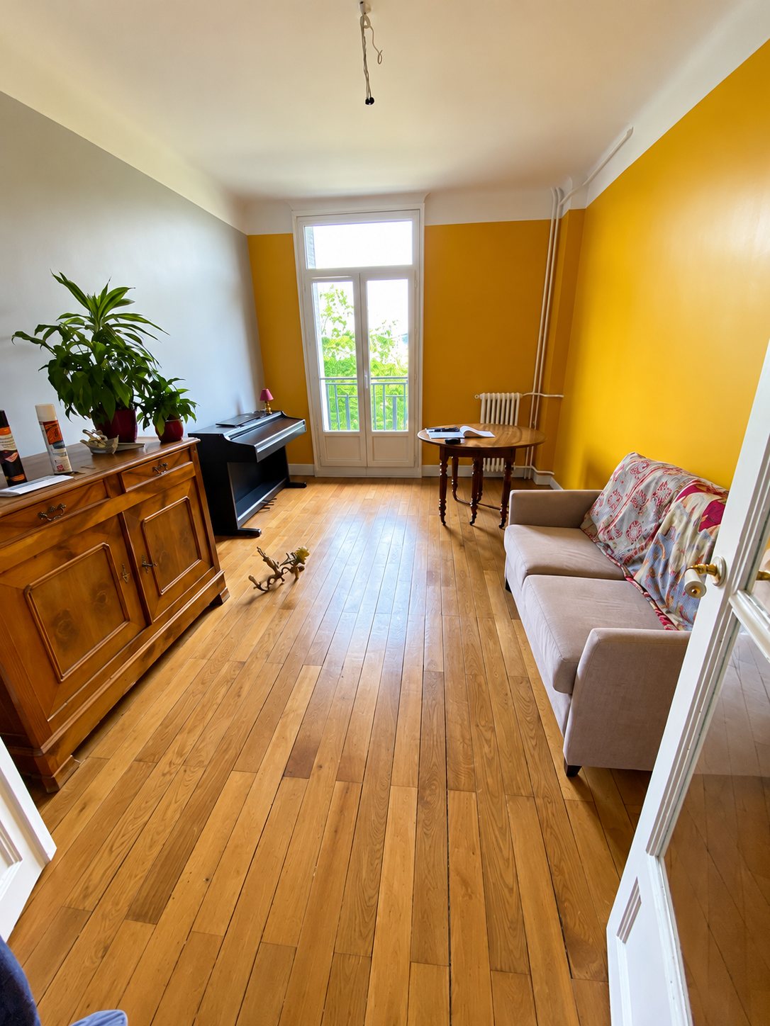 Salon lumineux avec parquet en chêne, murs jaune moutarde et piano numérique